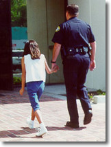 Law enforcement officer walking with child into a building. Children pictured are child actors.