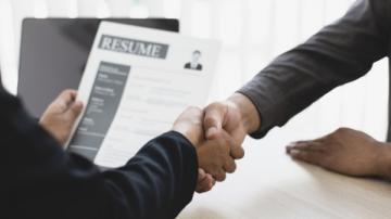 Two people shake hands while one reviews a resume 